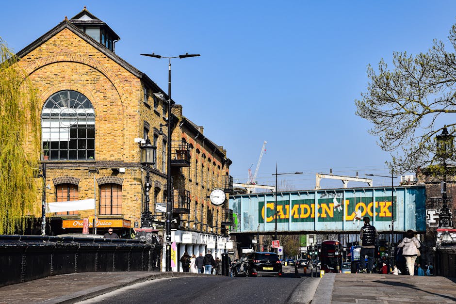 A street scene in Pentonville featuring a multi-story brick building with large arched windows and a clock mounted on the exterior wall. In the foreground, there are several pedestrians walking along